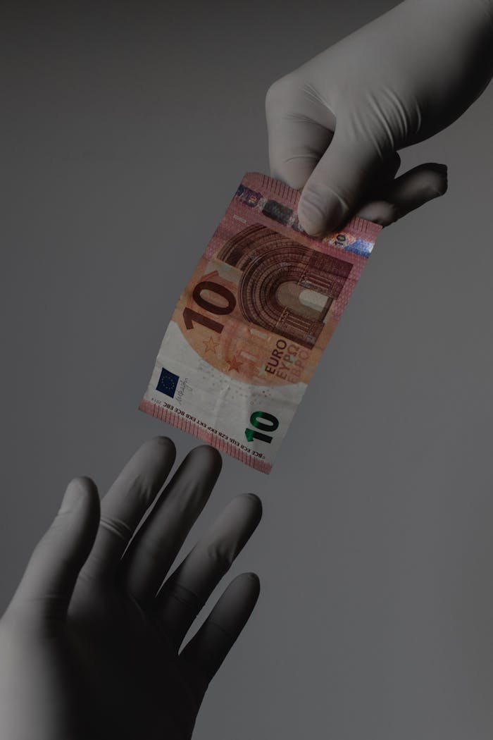about-02 Sterile transaction concept with gloved hands exchanging a 10 Euro note.